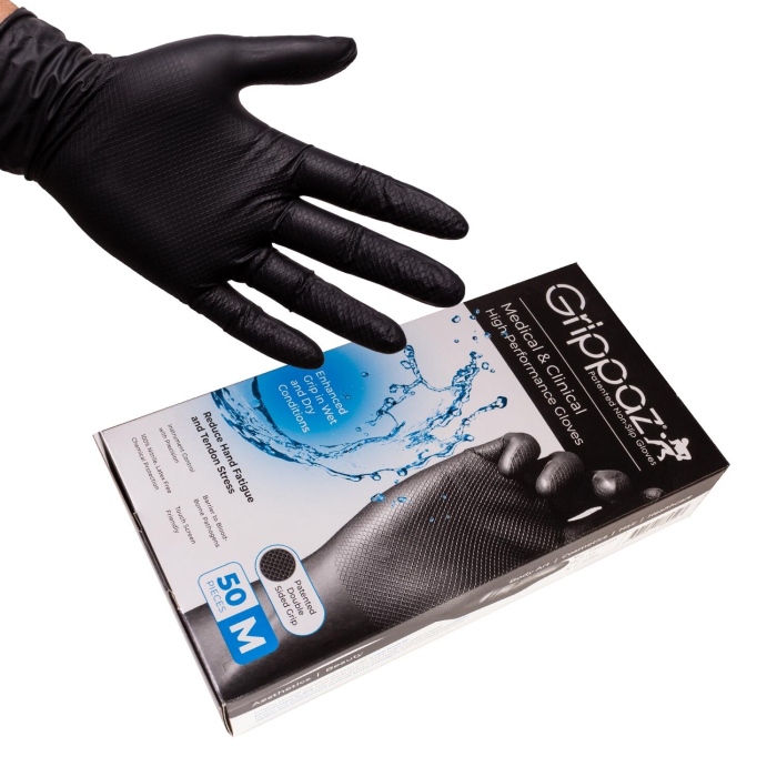 Une main portant un gant en nitrile texturé noir est représentée au-dessus d'une boîte étiquetée "Boite de 50 gants Grippaz - Gants antidrapants haute performance en nitrile - Noirs", qui contient 50 gants noirs antidérapants haute performance de taille m