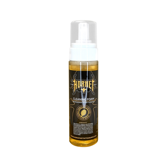 Un flacon de 220 ml de « Mousse de nettoyage pour tatouages Hornet », avec un bouchon transparent et un liquide ambré. L’étiquette blanche affiche la marque Hornet, les instructions d’utilisation et un emblème doré.